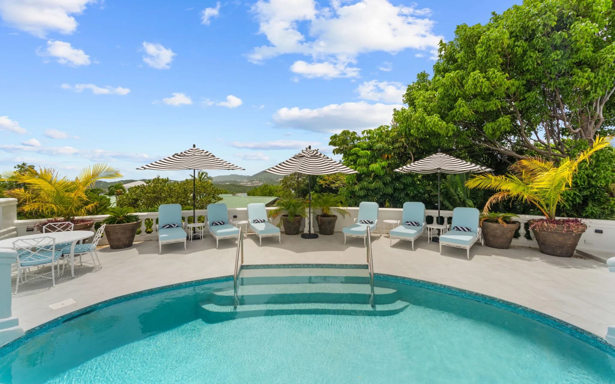 Curved private pool with striped umbrellas and loungers